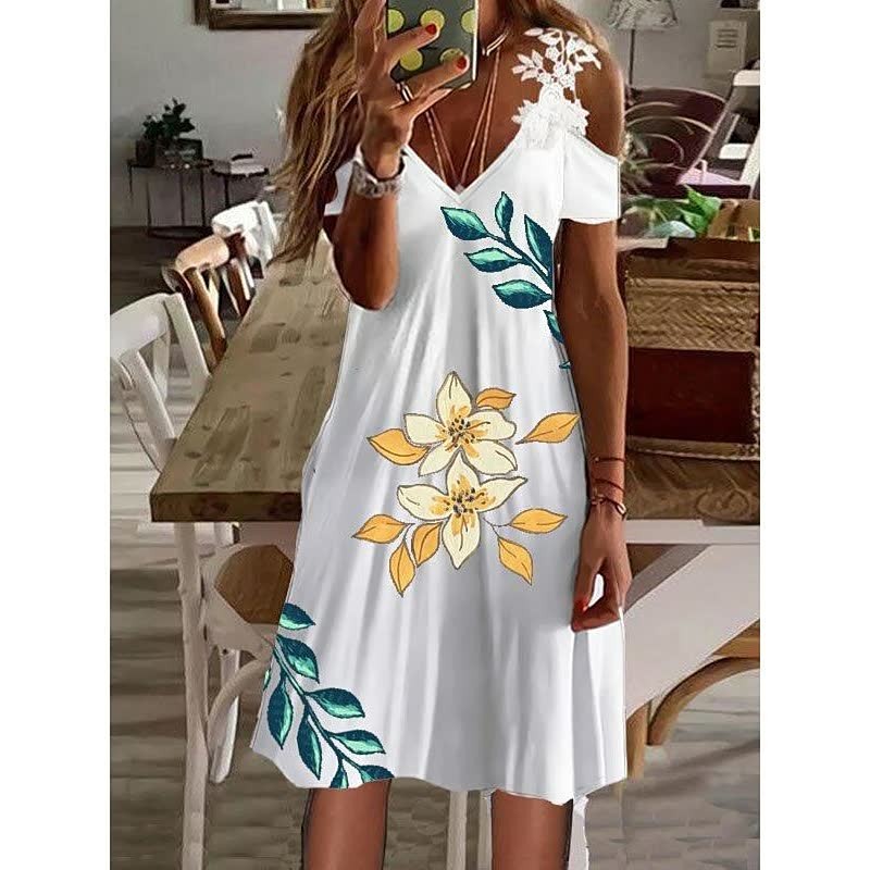 Frau in weißem Sommerkleid mit Blumenmuster, V-Ausschnitt, schulterfrei, im Wohnzimmer.
