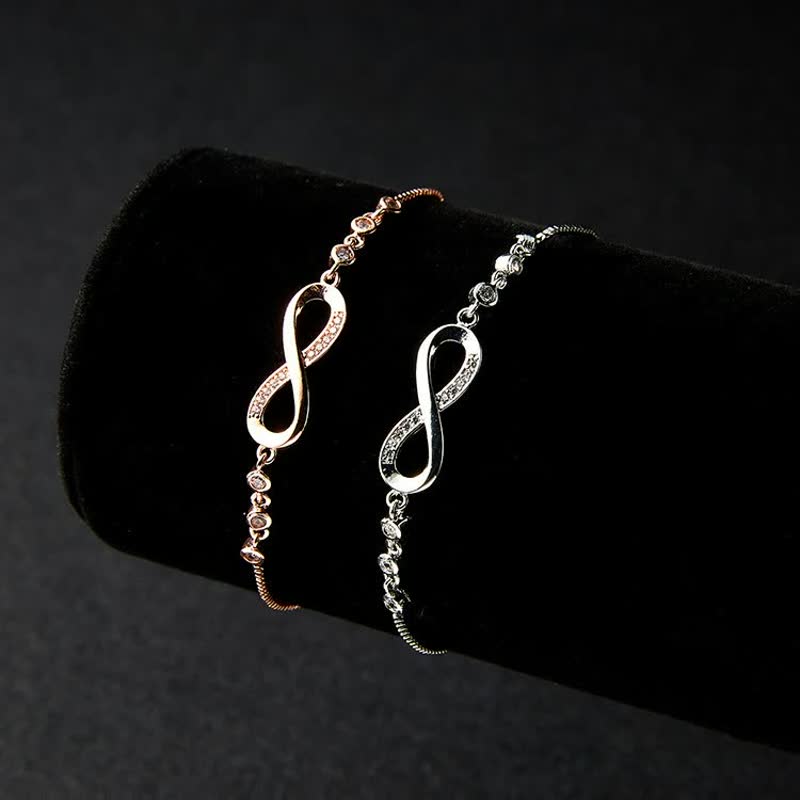 Zwei Infinity-Armbänder, roségold und silber, auf schwarzem Hintergrund, Schmuck, Damenaccessoire.