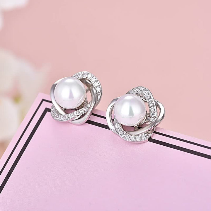 Silberne Ohrringe mit Perlen und Strasssteinen auf rosa Hintergrund, eleganter Schmuck.