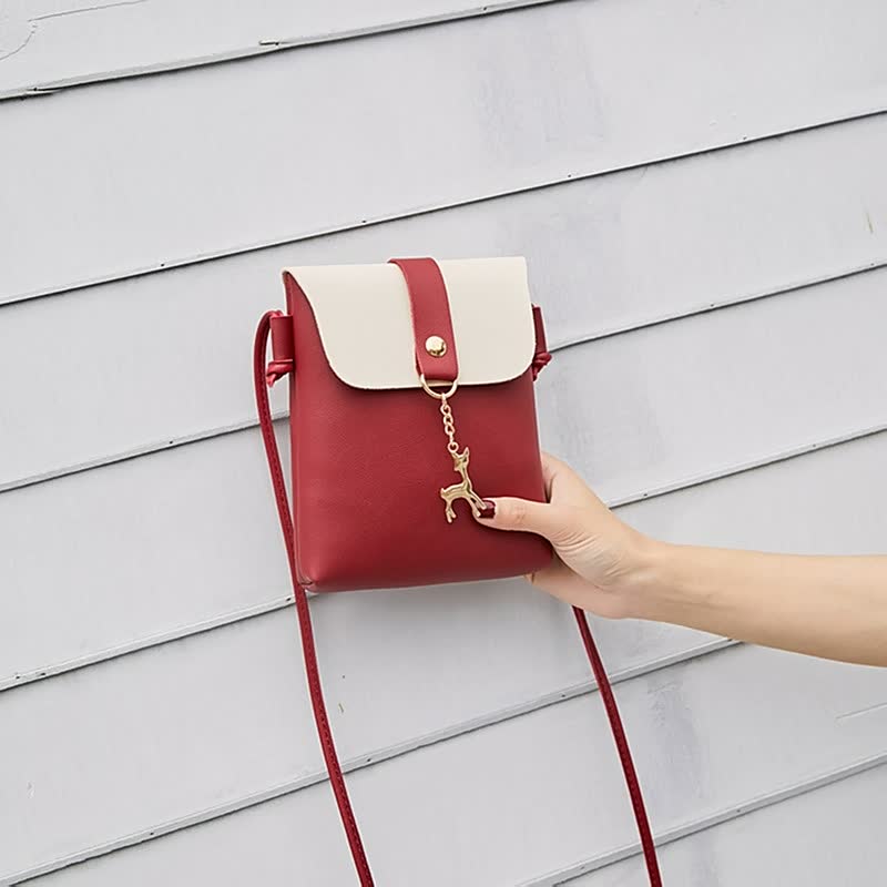 Rote Umhängetasche aus Leder mit weißem Verschluss und Hirschanhänger, Damenmode Accessoire.