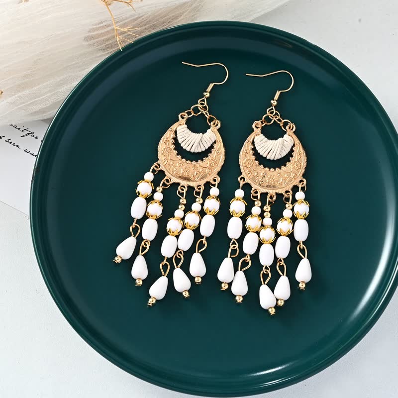 Goldene Ohrringe mit weißen Perlen, Boho-Stil, hängend, auf grünem Teller.