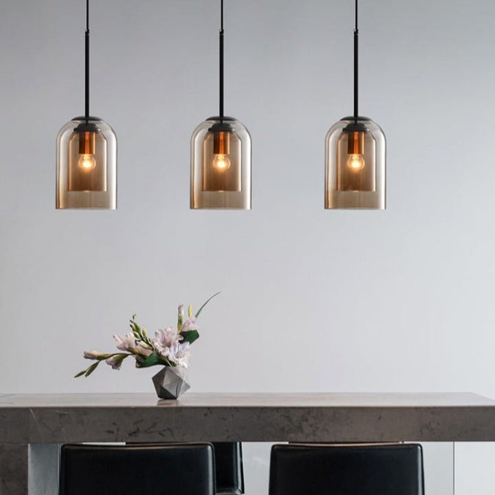 Drei moderne Pendelleuchten aus Glas über einem Esstisch mit Blumenarrangement.