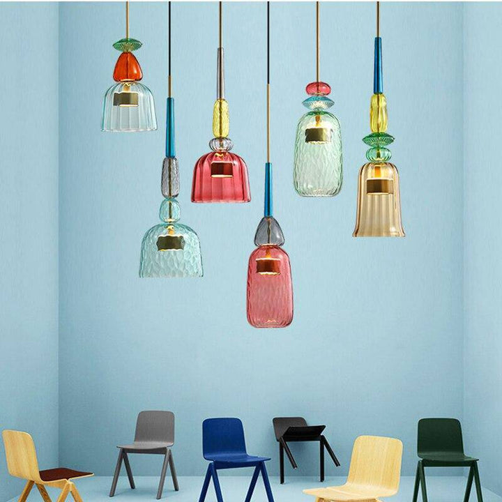 Bunte Glas-Pendelleuchten in modernem Design, hängend in einem Raum mit bunten Stühlen.