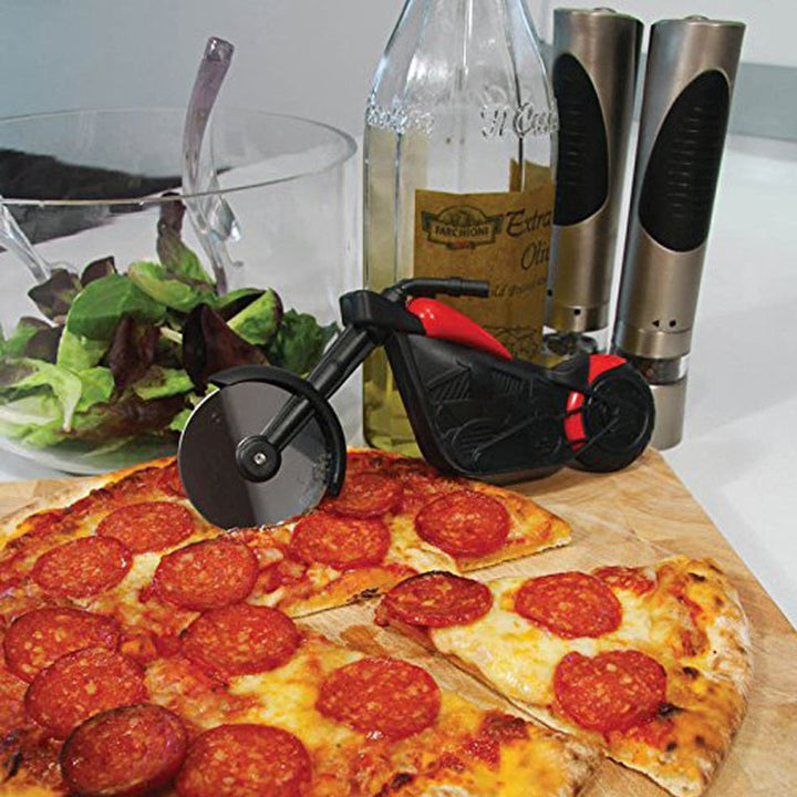 Motorrad-Pizzaschneider schwarz-rot, neben Salat und Pfeffermühlen auf Holzbrett.