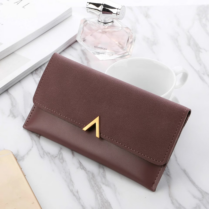 Lila Damen-Geldbörse aus Leder mit goldener Schnalle auf Marmortisch, stilvoll und elegant.