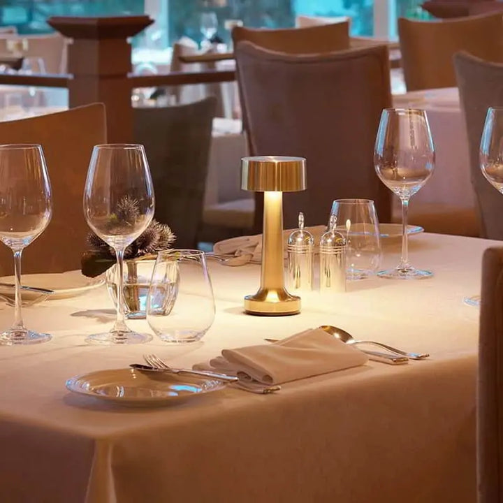 Elegante Tischlampe aus Messing auf gedecktem Restauranttisch mit Weingläsern und Besteck.