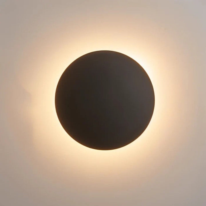 Tmavě hnědý až černý kulatý disk na zdi s teplou září kolem okraje 2