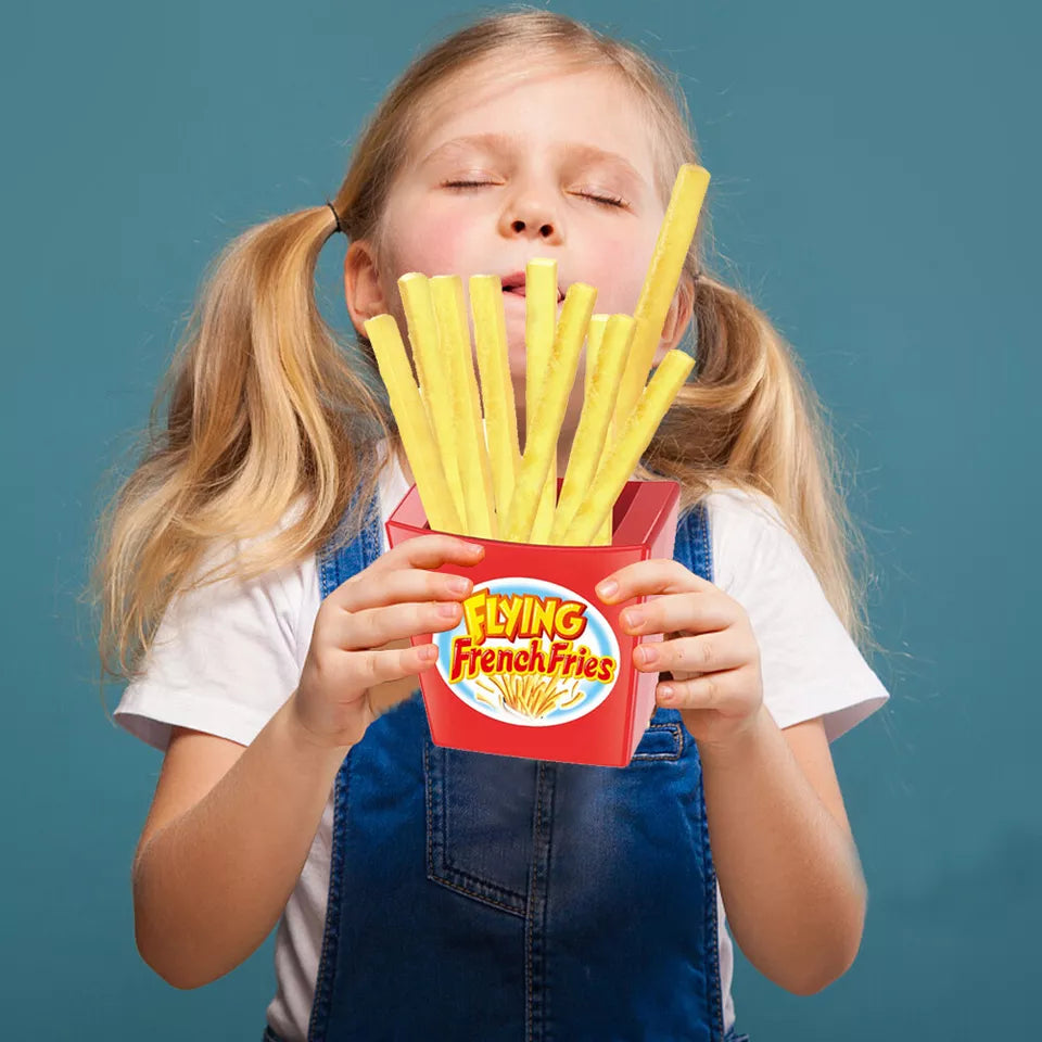 Mädchen mit blonden Zöpfen hält rote Box mit langen gelben Pommes Frites vor blauem Hintergrund.