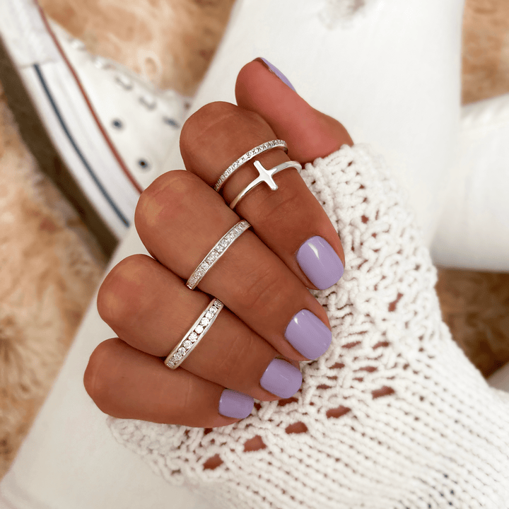 Frau mit lila Nagellack trägt silberne Ringe, Kreuzdesign, gestrickter weißer Pullover.