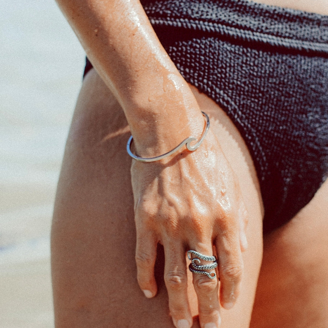 Silberarmband am Handgelenk einer Frau am Strand, elegantes Schmuckdesign, Sommermode.
