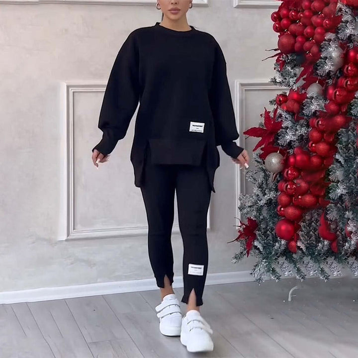 Frau in schwarzem Oversize-Pullover und Leggings, weiße Sneaker, neben Weihnachtsbaum.