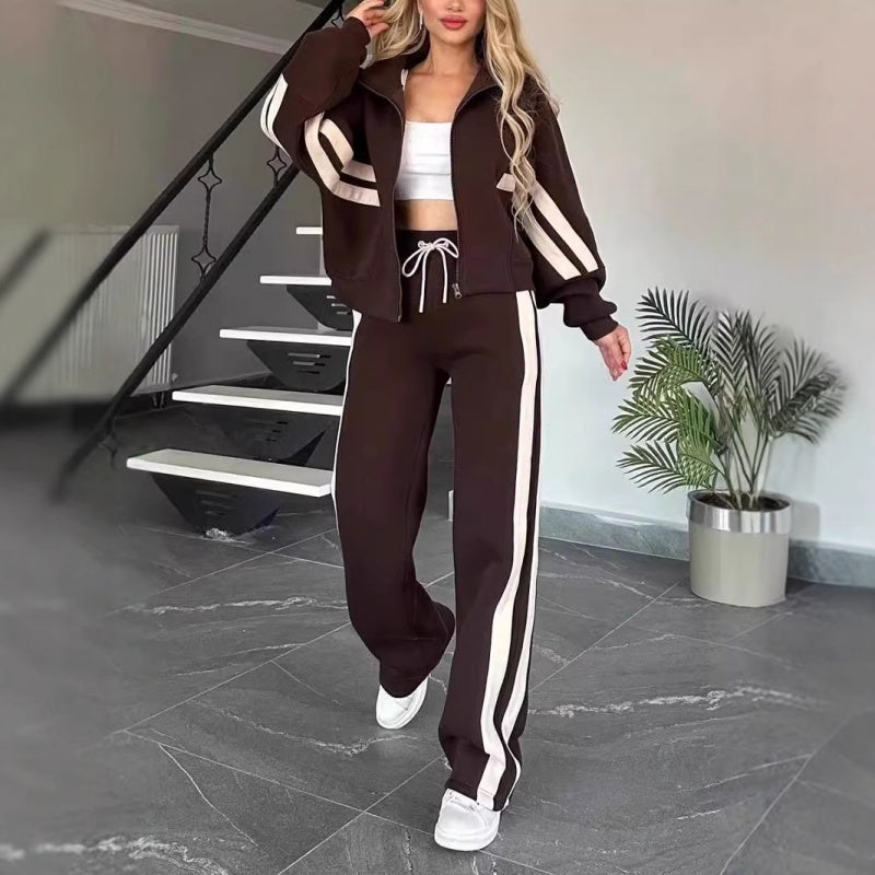 Souprava v tmavě hnědé barvě s krémovými pruhy, modelka kráčí po místnosti, bunda na zip a široké kalhoty s bílou šňůrkou. 8