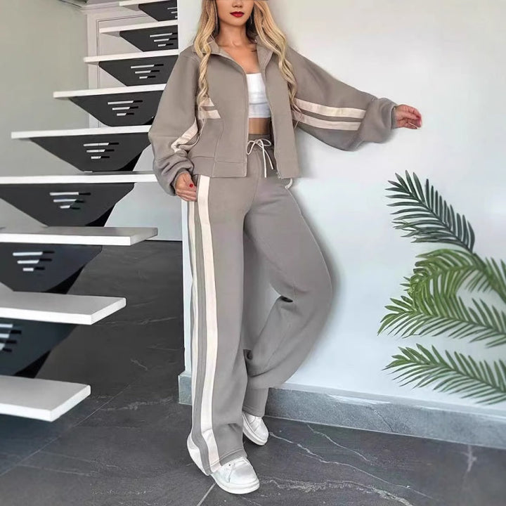 Šedá souprava s béžovými pruhy, modelka se opírá o zeď vedle schodů, bunda s širokými rukávy a volné kalhoty. 6