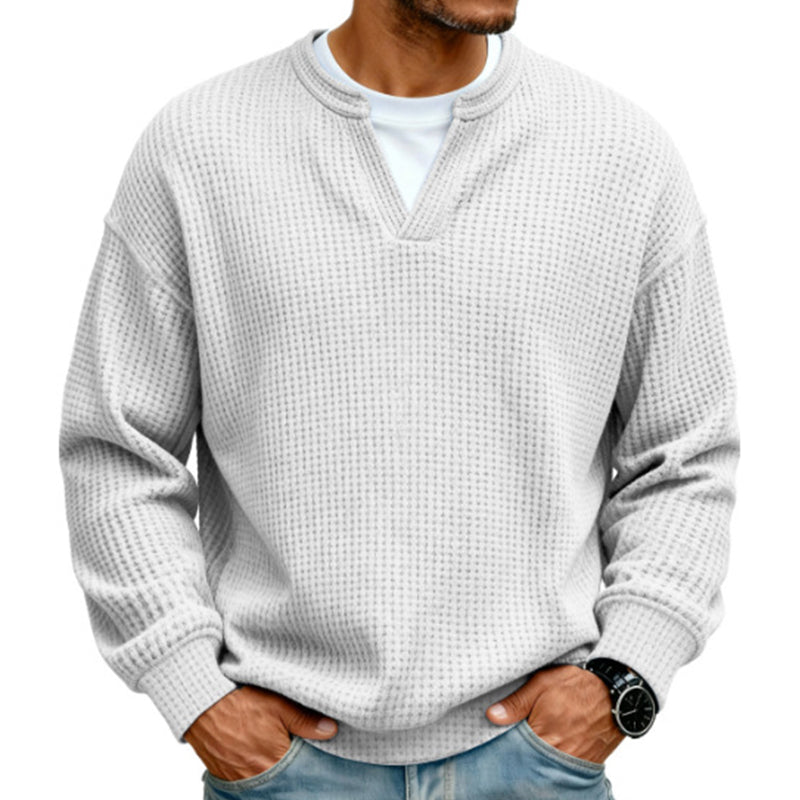 Světle šedobílý vaflový svetr s výstřihem do véčka a bílým trikem pod ním, nošený mužem s džínami. 14