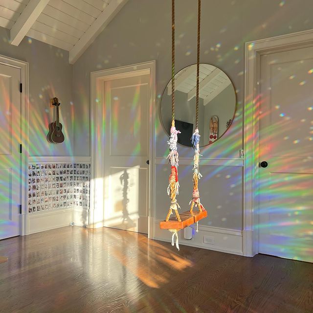Bunter Suncatcher im Raum, Regenbogenlicht, hölzerner Boden, dekorativer Spiegel, Gitarre an Wand.