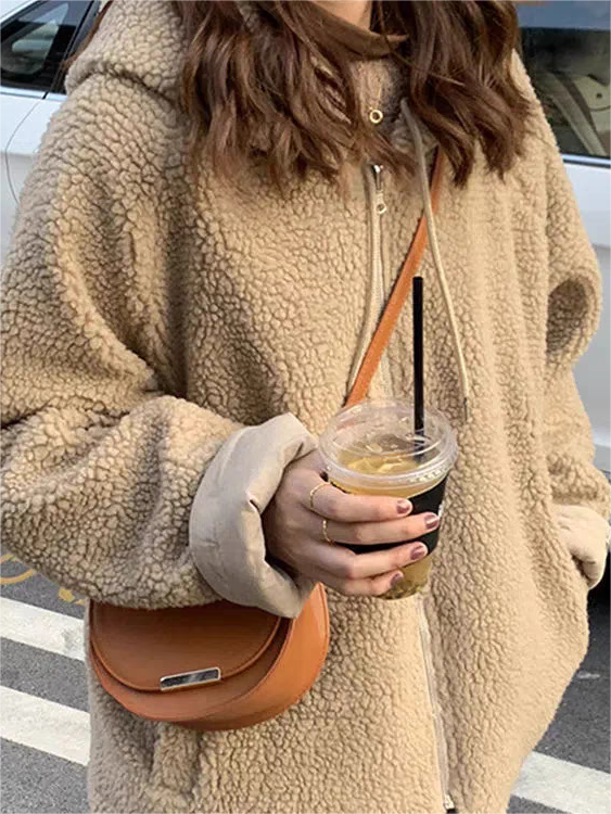 Frau in beigem Teddyfell-Mantel mit brauner Umhängetasche und Eiskaffee auf der Straße.