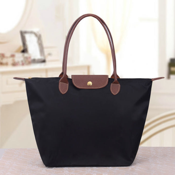 Schwarze Handtasche aus Leder und Nylon mit braunen Griffen auf einem Tisch im eleganten Raum.