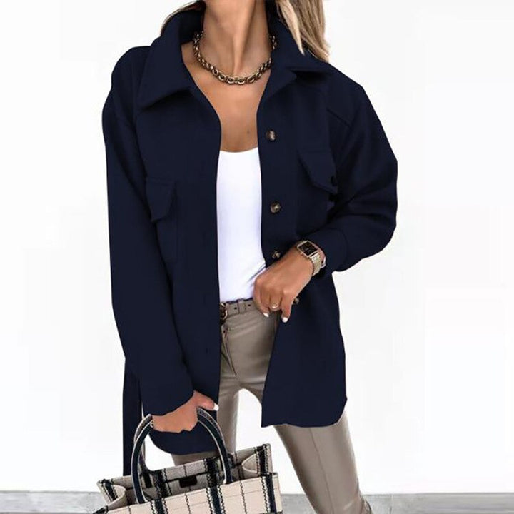 Frau in marineblauer Jacke, weißem Top, Lederhose, hält karierte Tasche, modisch, elegant.
