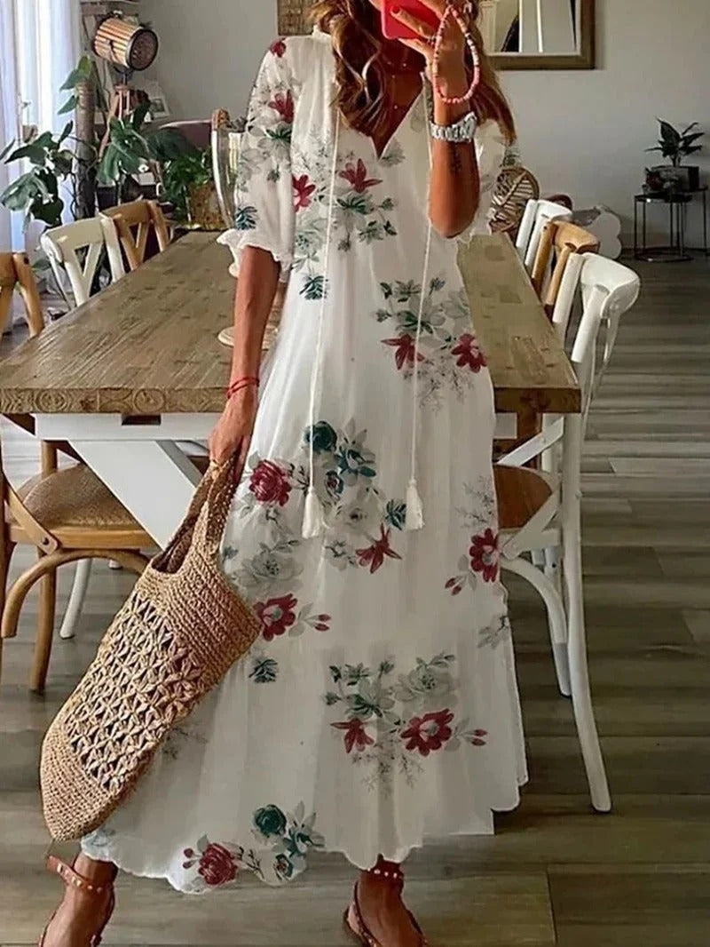 Frau in weißem, geblümtem Maxikleid mit Strohtasche in modernem Esszimmer.