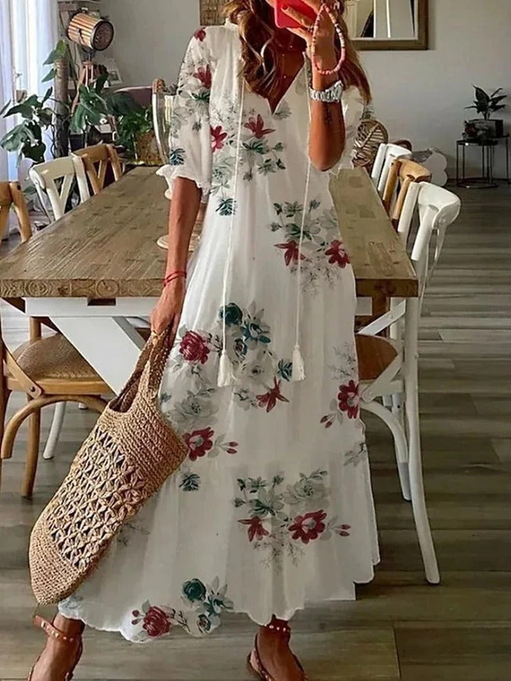 Frau in weißem, geblümtem Maxikleid mit Strohtasche in modernem Esszimmer.