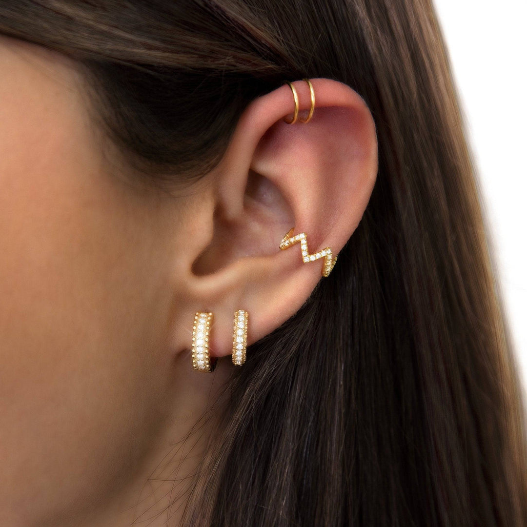 Frau mit goldenen Ohrringen, Zickzack-Design, Perlenbesatz, modischer Schmuck, Nahaufnahme.