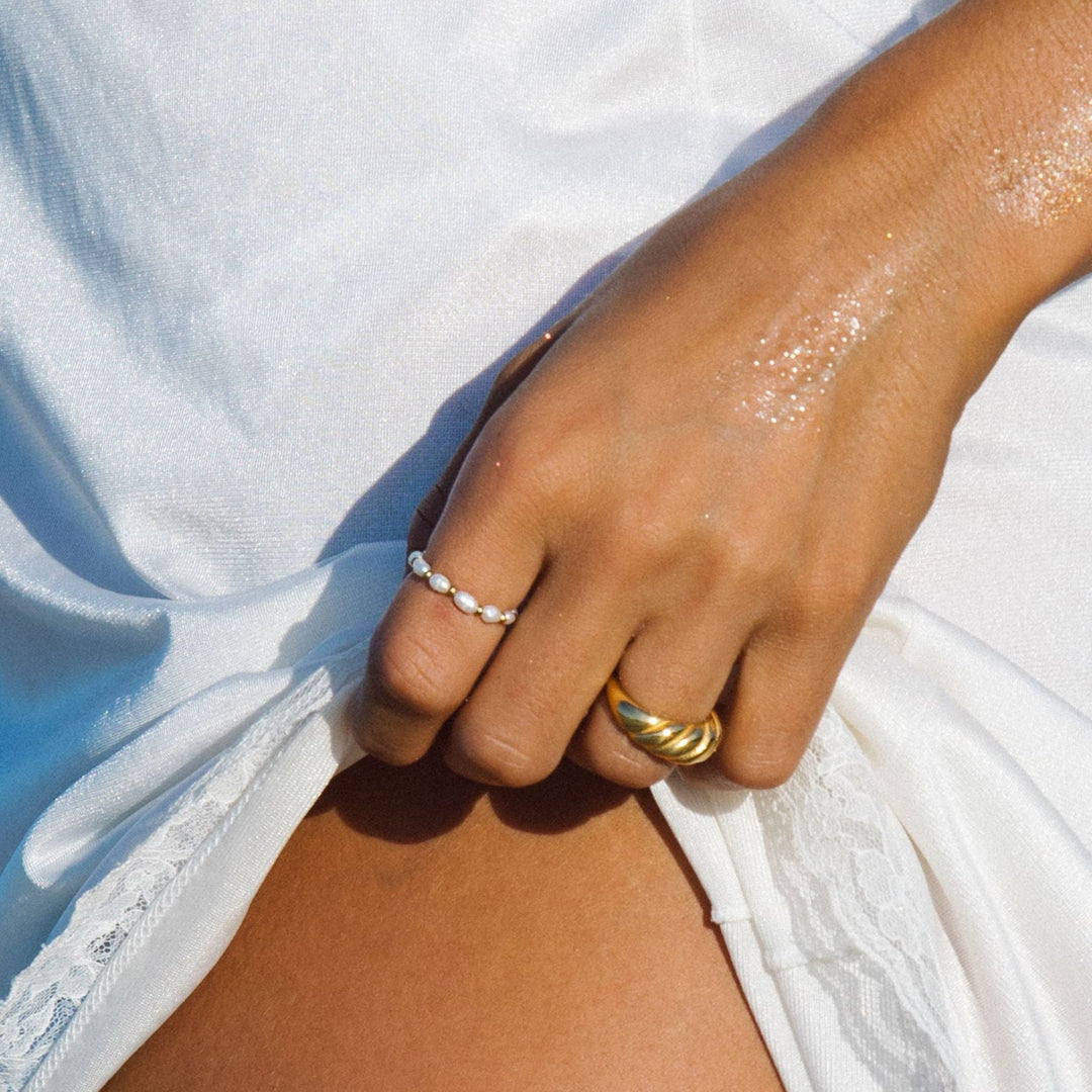 Hand mit wasserdichten Ringen, Gold und Perlen, auf weißem Stoff.