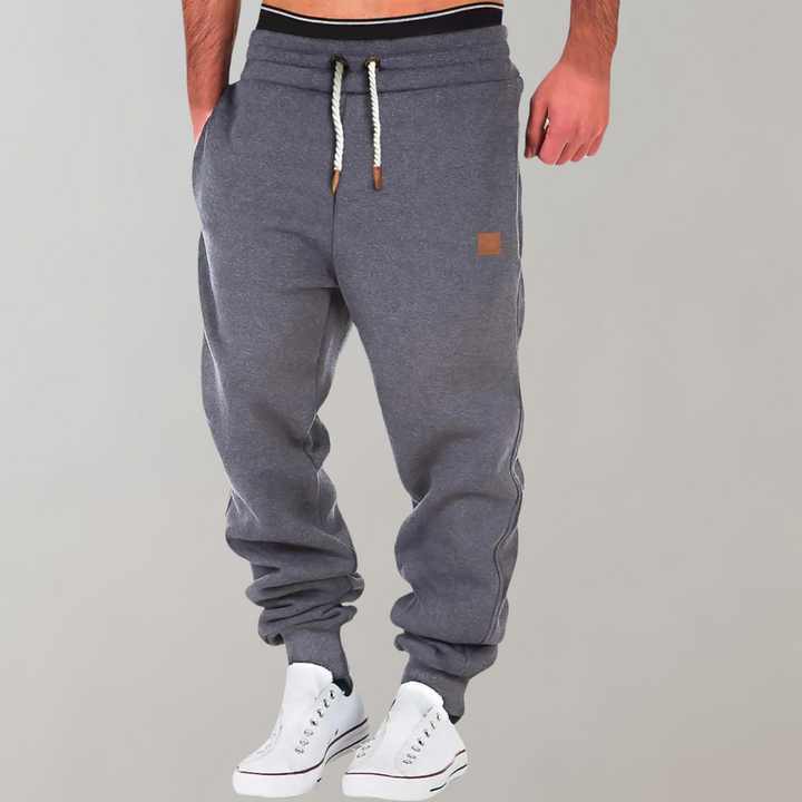 Šedé jogger kalhoty s bílou šňůrkou v pase na modelovi, ruka v kapse 2