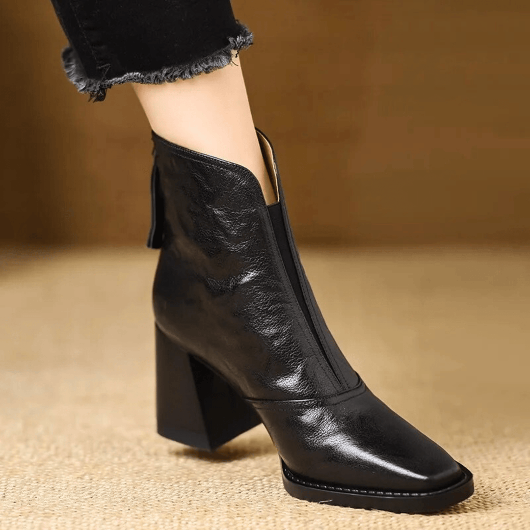 Černá lesklá kožená kotníková bota s hranatou špičkou a širokým podpatkem na noze modelky 2