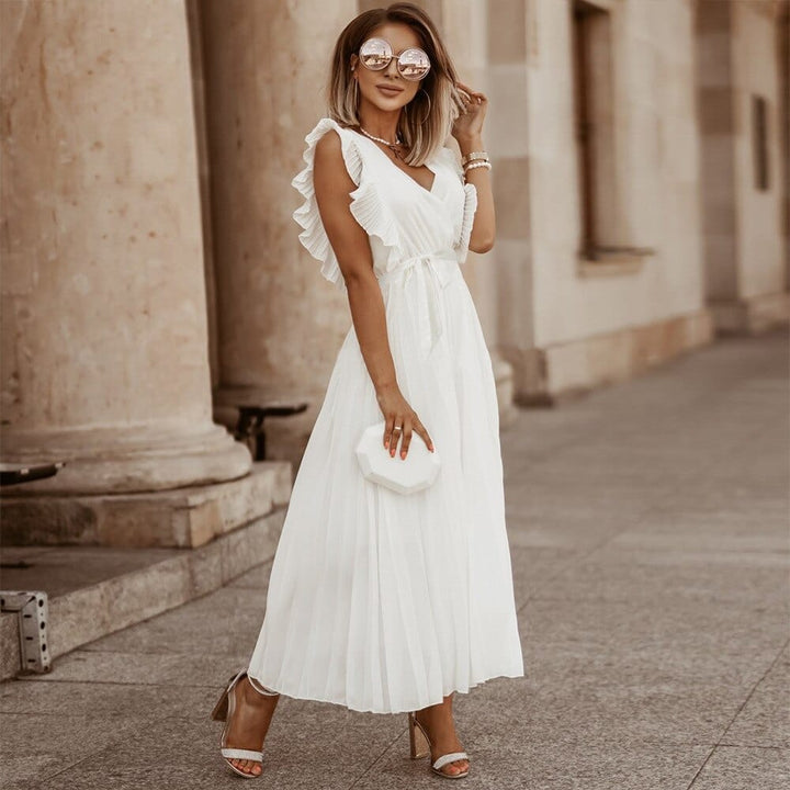 Frau in weißem, boho Brautkleid mit V-Ausschnitt, Sonnenbrille und Handtasche, elegant gekleidet.