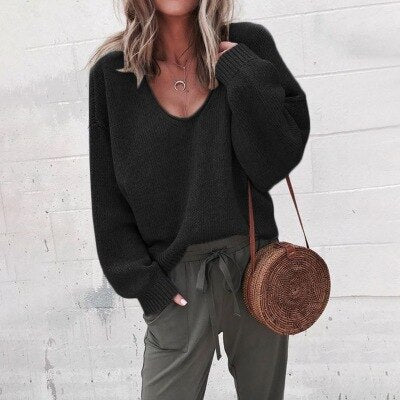 Frau in schwarzem V-Ausschnitt Strickpullover, olivgrüne Hose, runde Strohtasche.