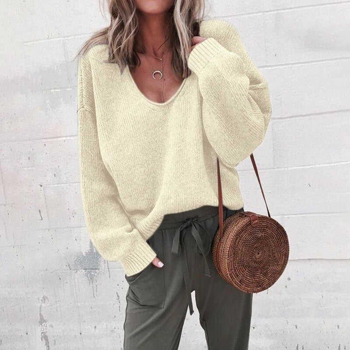 Frau in cremefarbenem V-Ausschnitt Strickpullover, grüne Hose, runde Strohtasche.