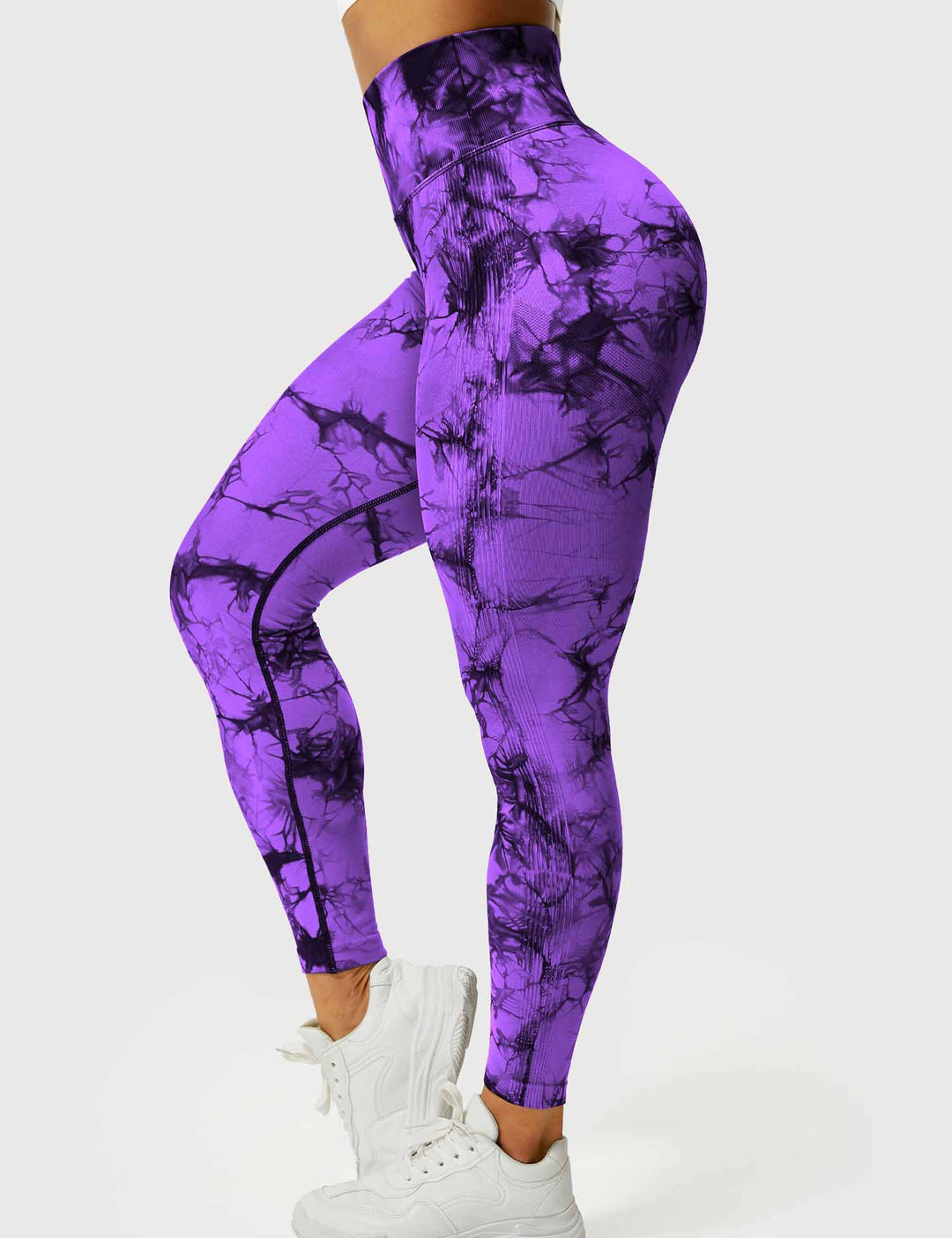 Frau in lila Batik-Leggings, hohe Taille, Sportmode, Fitnessbekleidung, weiße Turnschuhe.