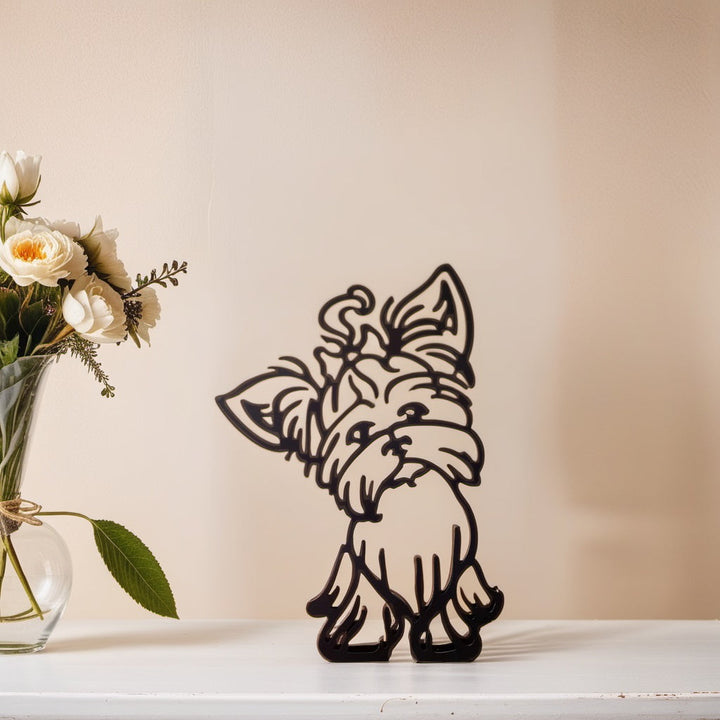 Metall-Wanddekoration Yorkshire Terrier, schwarz, auf weißem Tisch, neben Blumenstrauß in Vase.